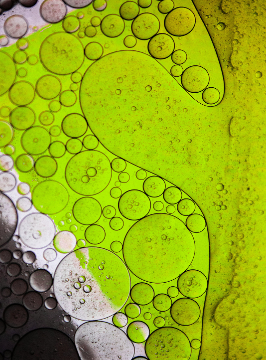 Macro shot of oil and water patterns in vibrant green and black, forming organic shapes.