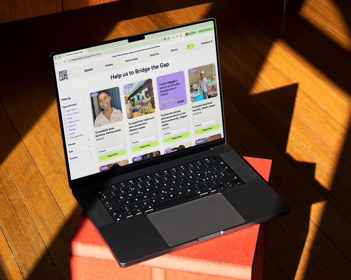 Laptop auf einem roten Stuhl, auf dem die Spendenplattform Bridging Gaps zu sehen ist. Unternehmerprofile und Spendenoptionen sind auf dem Bildschirm sichtbar.