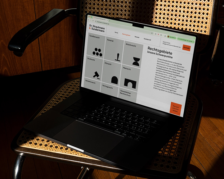 Ein Laptop auf einem gewebten Stuhl, auf dem die Website der Anwaltskanzlei angezeigt wird und einen Überblick über die Bereiche der Rechtspraxis zeigt, die durch minimalistische schwarze Symbole auf grauem Hintergrund dargestellt werden.