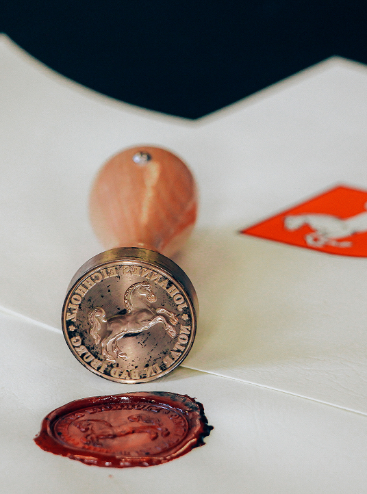 Neben einem roten Wachssiegel befindet sich ein Notarstempel mit einem Pferdeemblem, das die Verbundenheit der Firma zu Tradition, Authentizität und rechtlicher Autorität unterstreicht.
