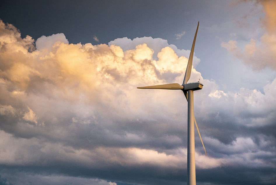 Eine Windkraftanlage steht hoch vor einem dramatischen bewölkten Himmel bei Sonnenuntergang und symbolisiert erneuerbare Energien und Nachhaltigkeit.