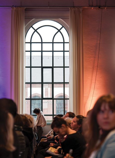 Konferenzpublikum bei der Veranstaltung Stellung beziehen, Demokratie verteidigen! Museen in Zeiten politischen Drucks in einer Halle mit Bogenfenstern.