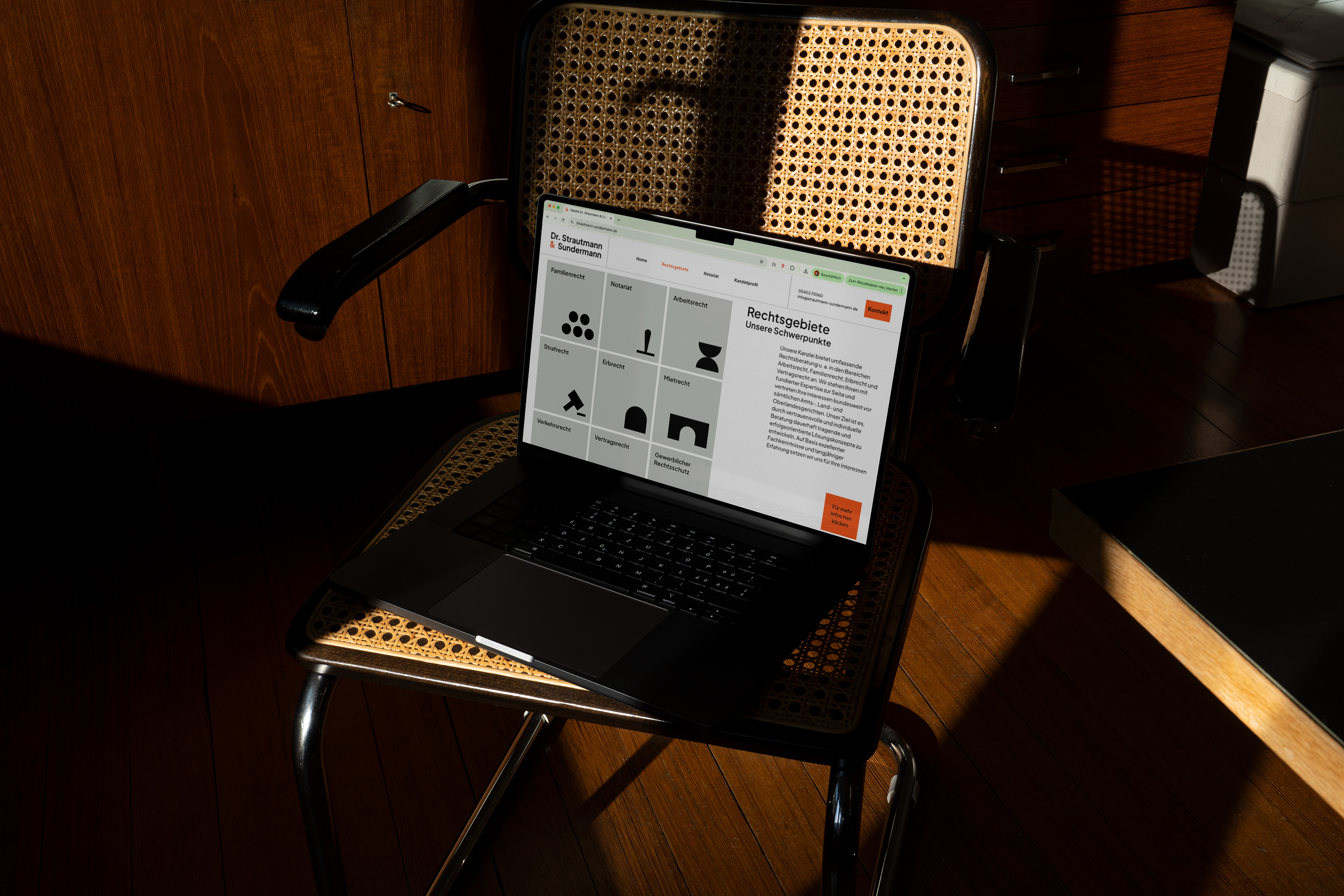 Ein Laptop auf einem gewebten Stuhl, auf dem die Website der Anwaltskanzlei angezeigt wird und einen Überblick über die Bereiche der Rechtspraxis zeigt, die durch minimalistische schwarze Symbole auf grauem Hintergrund dargestellt werden.