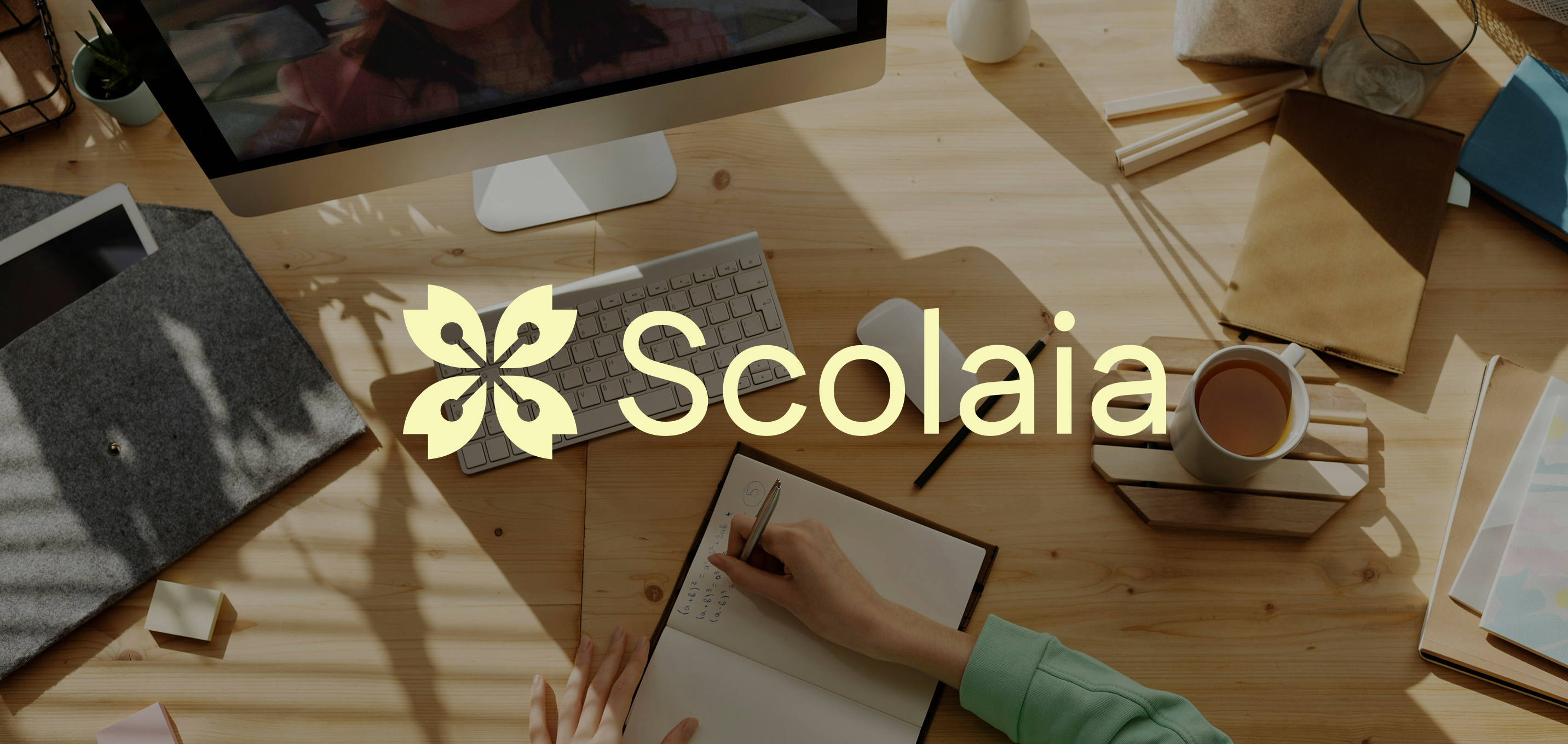 Large Scolaia logo with logo mark over workspace scene with computer and notebook