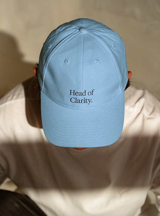Person, die eine hellblaue Baseballkappe trägt, auf der Vorderseite der Text „Head of Clarity.“ aufgestickt ist.