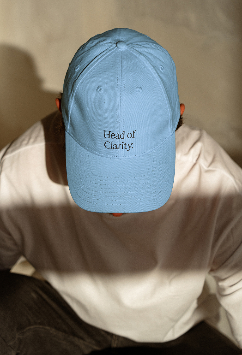Person, die eine hellblaue Baseballkappe mit dem aufgestickten Text „Head of Clarity.“ auf der Vorderseite trägt, trägt ein weißes Hemd.