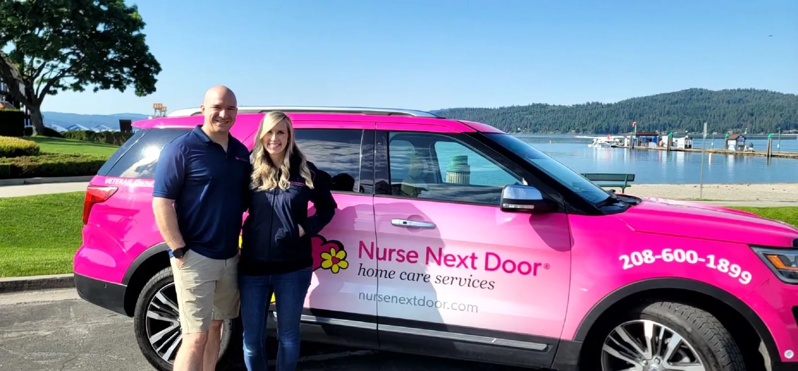 Two Nurse Next Door franchise owners standing beside a pink company car in front of a historic building, symbolizing financial support and success in franchising.
