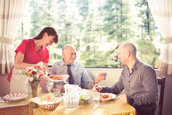 A smiling Nurse Next Door Caregiver serving food to a father and son