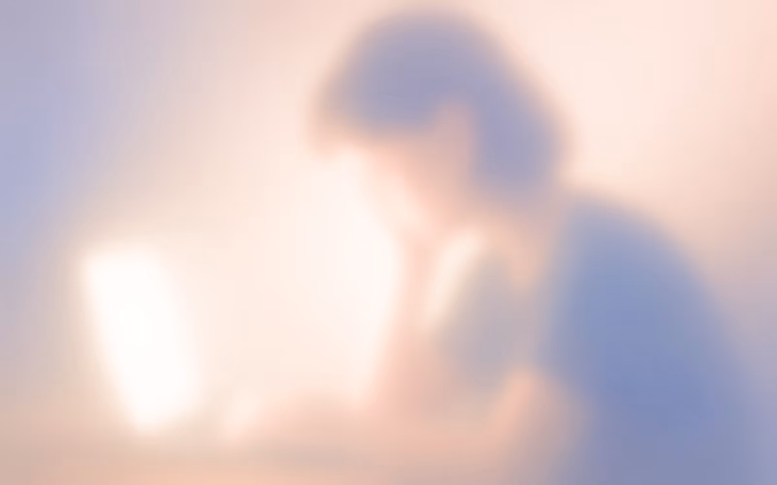 Dreamy blurred illustration of a tired creative working late at a desk with a glowing laptop, representing burnout, drained energy, and overwork in soft pastel colors.