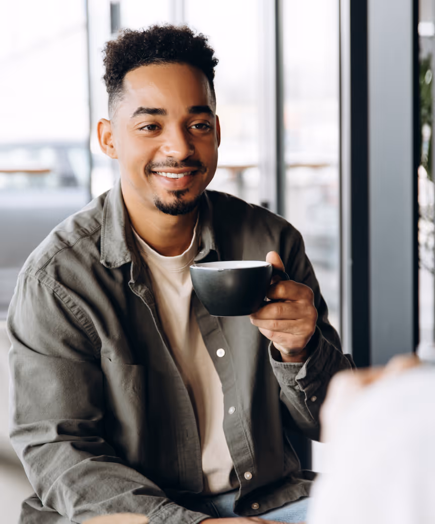 Young man sitting sipping coffee smiling and while talking with an Tax advisor.