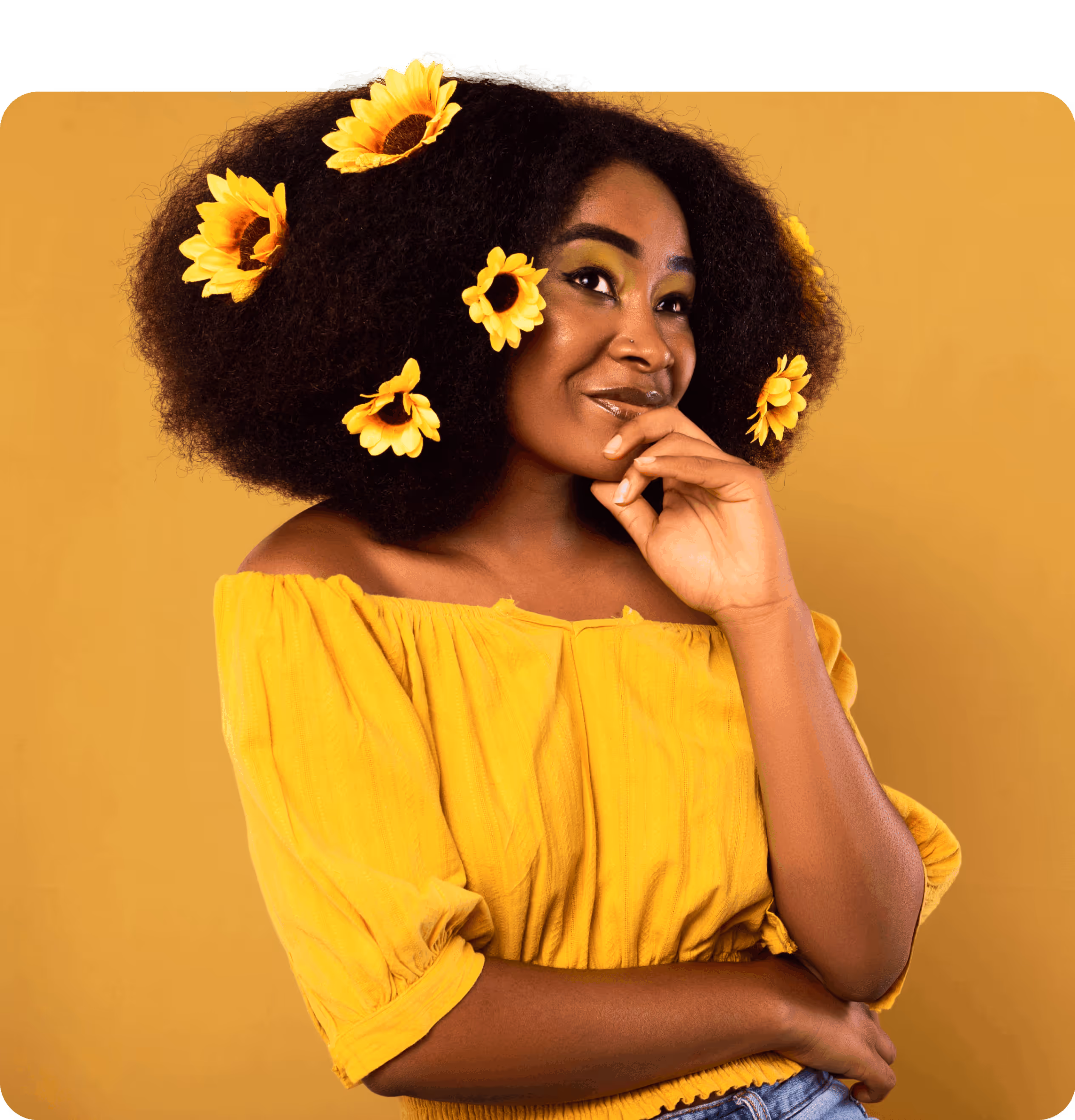 Dark skin girl sitting with sunflower in her afro hair smiling with a thoughtful look.
