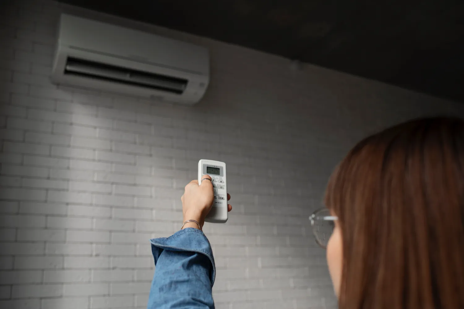 Person adjusting air conditioning remote control near wall-mounted unit
