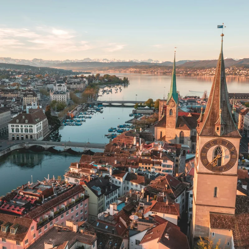 Luftaufnahme von Zürich mit Kirchturm und Alpenkette im Hintergrund