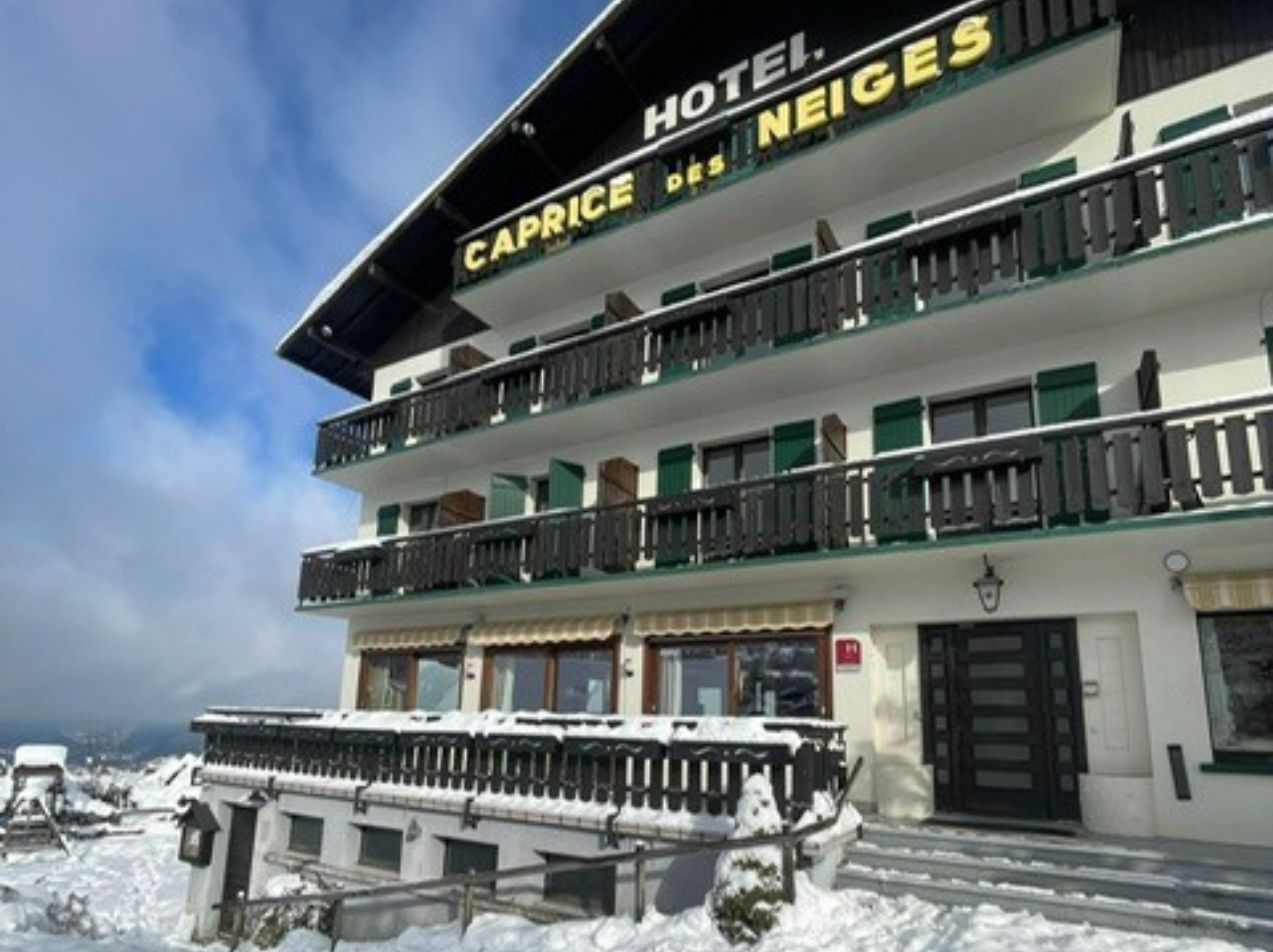 Hotel Caprice des Neiges in Combloux under a blanket of snow, side façade with balcony and snow-covered landscape