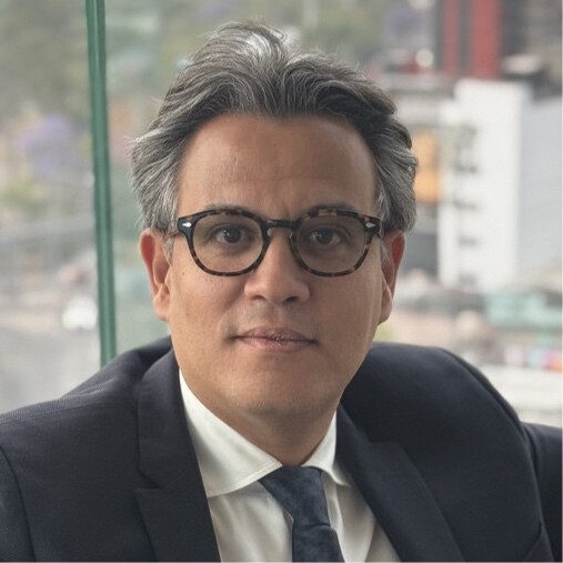 Homme souriant portant des lunettes et une chemise noire, bras croisés.