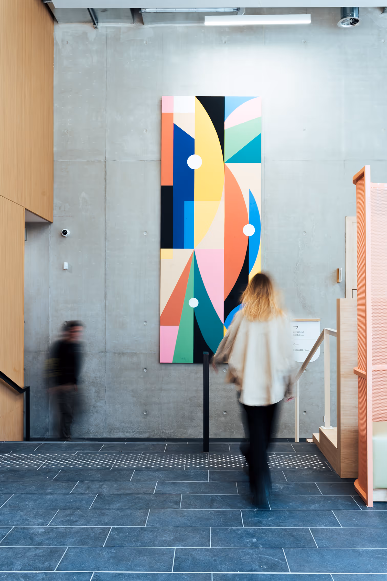 Blurred people walking in a modern interior space with a large colorful abstract painting hanging on a concrete wall.