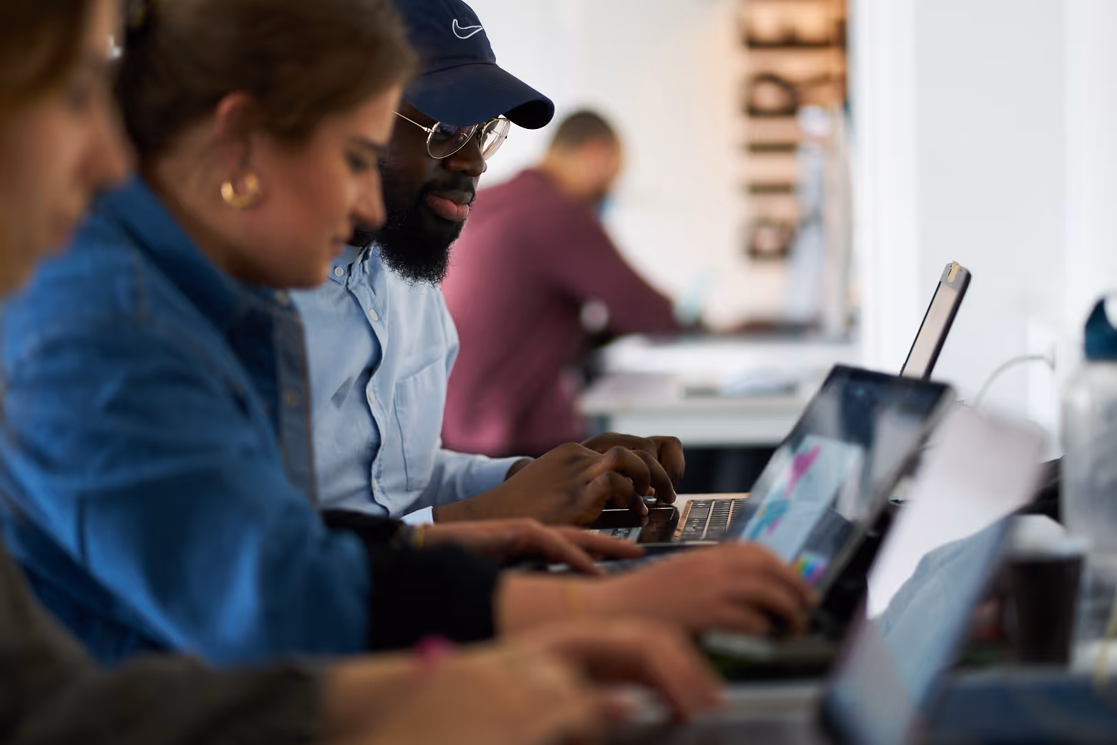 Four people working focused on their laptops in a bright office.