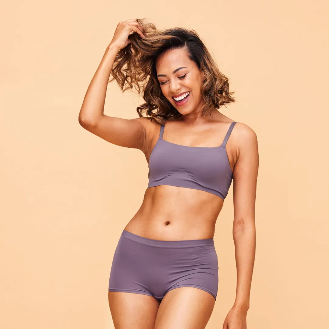 Smiling woman in a purple bikini set against a peach background.