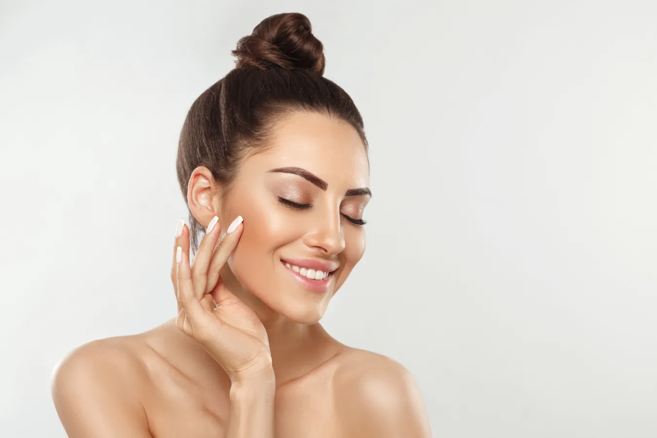 Smiling woman with natural makeup touching her face.
