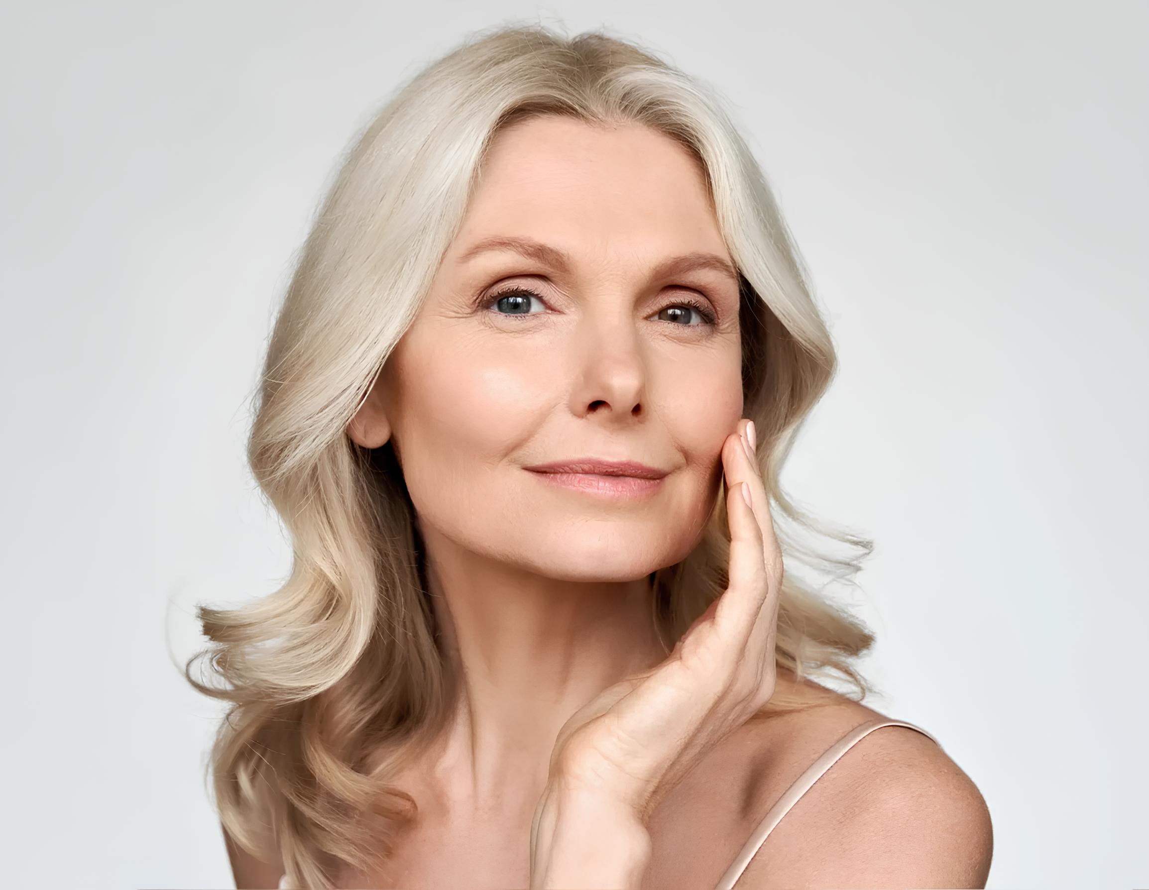 Portrait of an older woman with soft features and a gentle smile, touching her face.