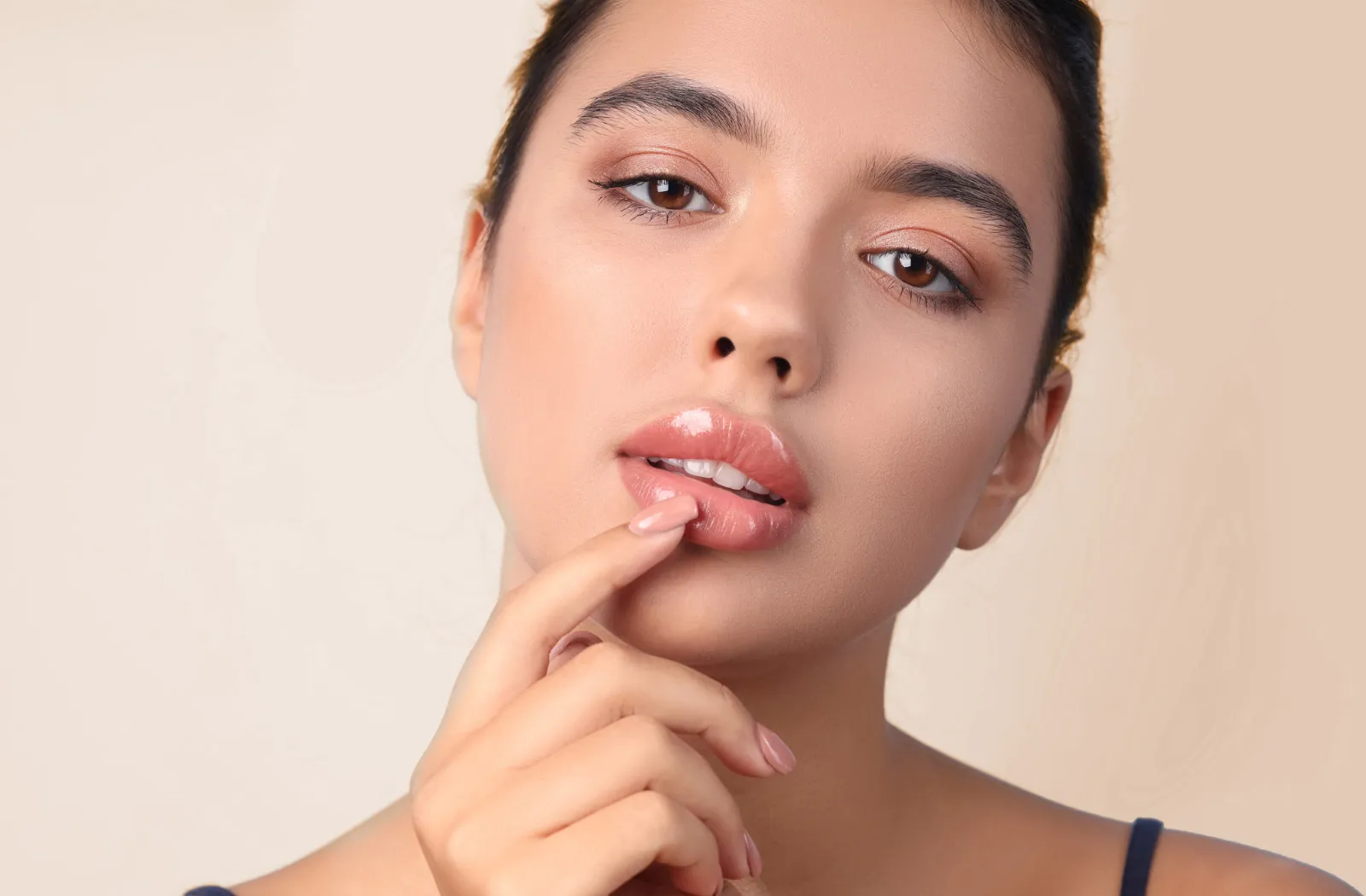 Young woman touching her lips with a neutral background.