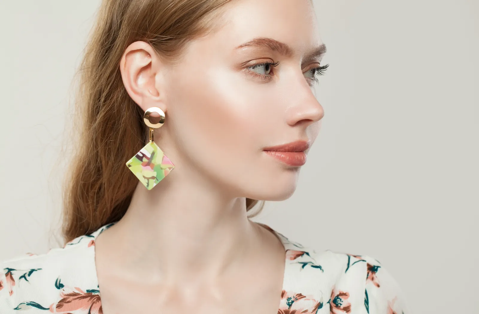 Woman in floral blouse wearing geometric earrings, looking sideways, against a neutral background.