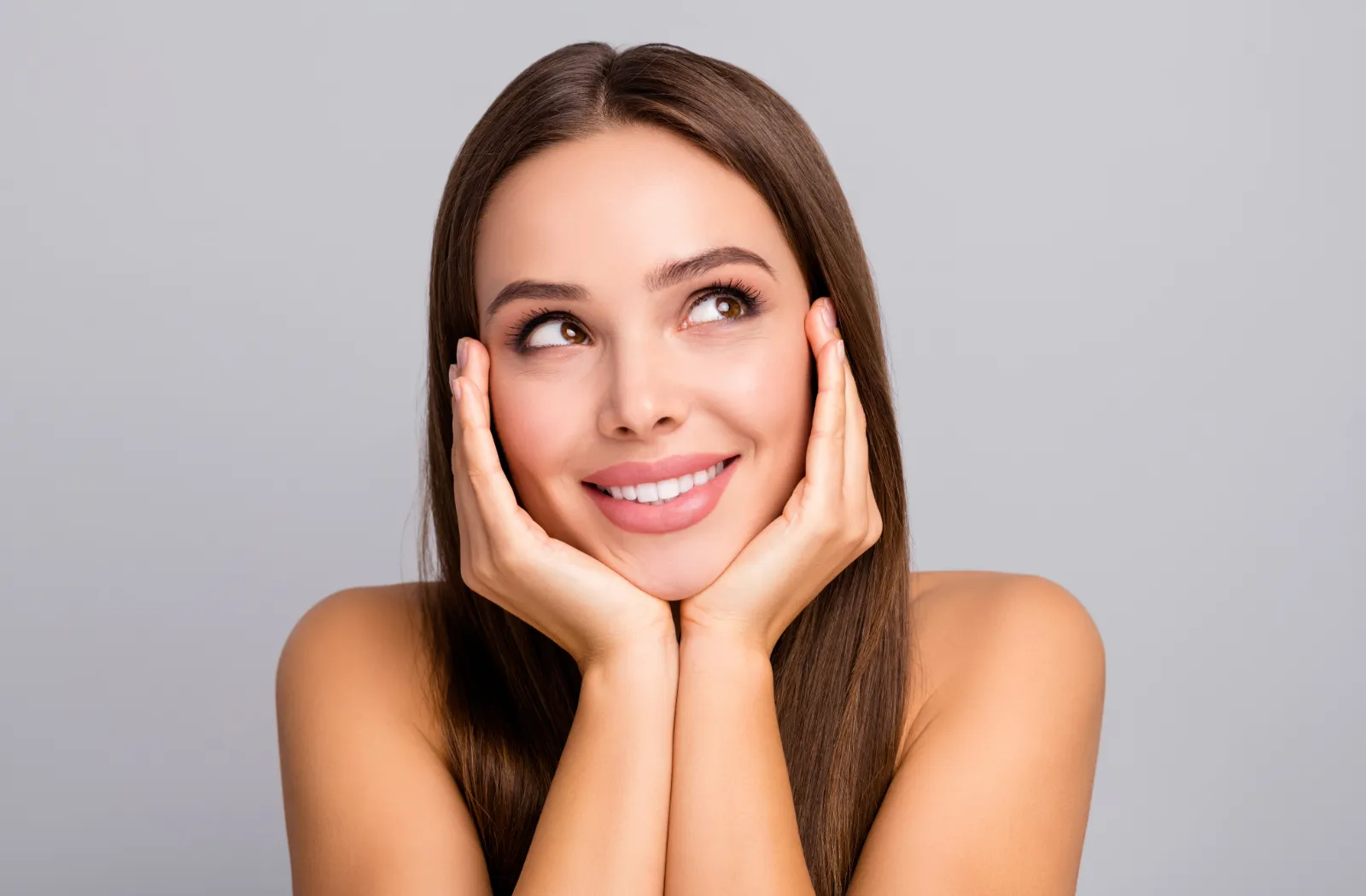 Smiling woman resting her chin on hands against a gray background.