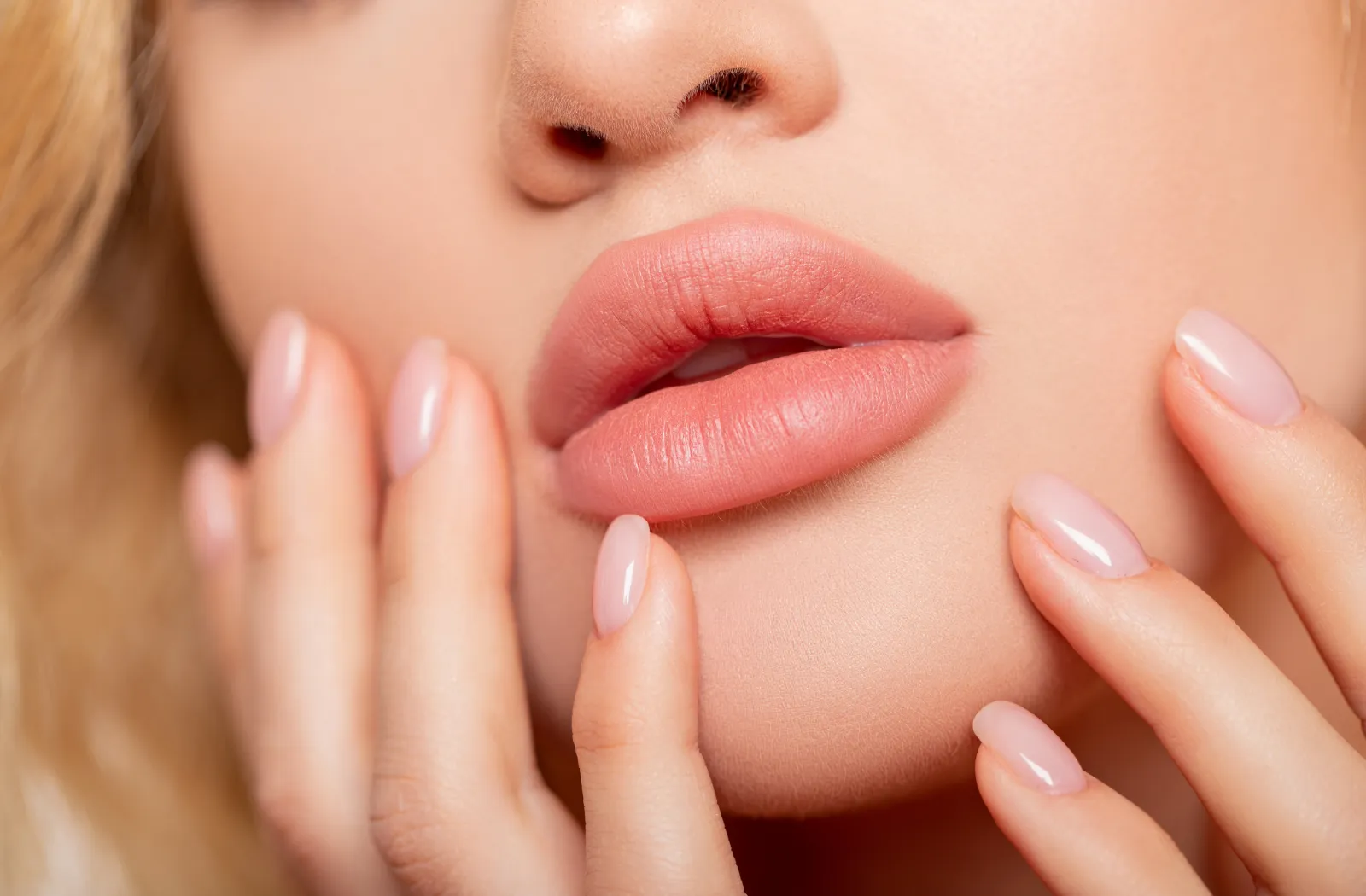 Close-up of woman’s lips and hands, showcasing natural-looking lip enhancement.