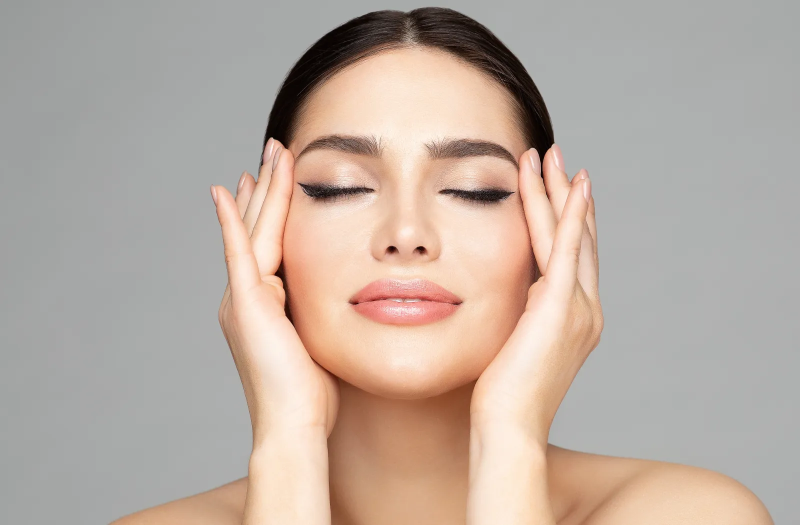 Woman with closed eyes and hands on her face, showcasing a natural beauty look.