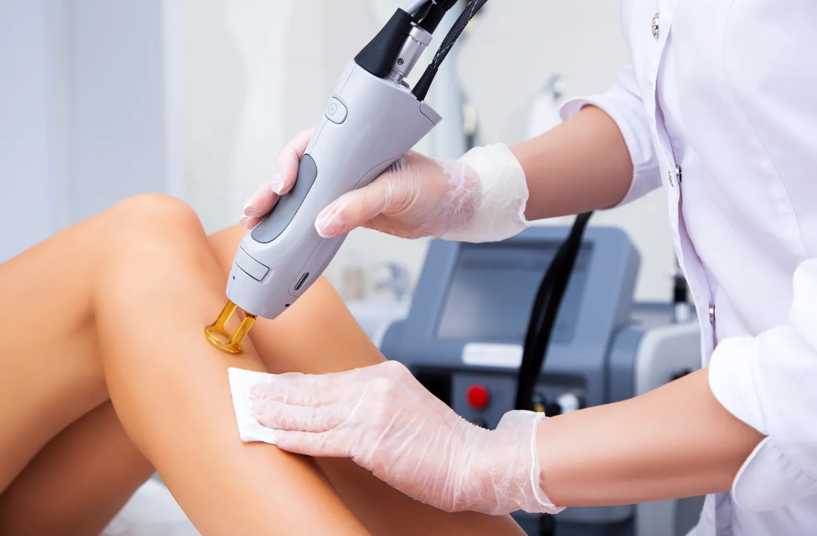 Technician performing laser hair removal on a patient's leg in a clinic setting.