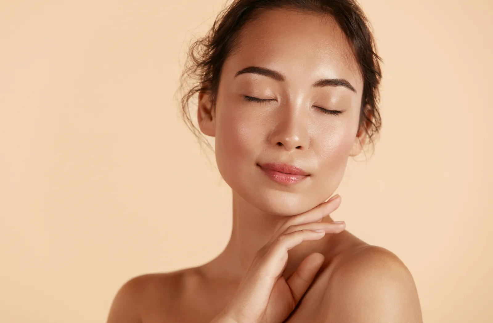 Woman with closed eyes and serene expression, touching her face against a soft beige background.