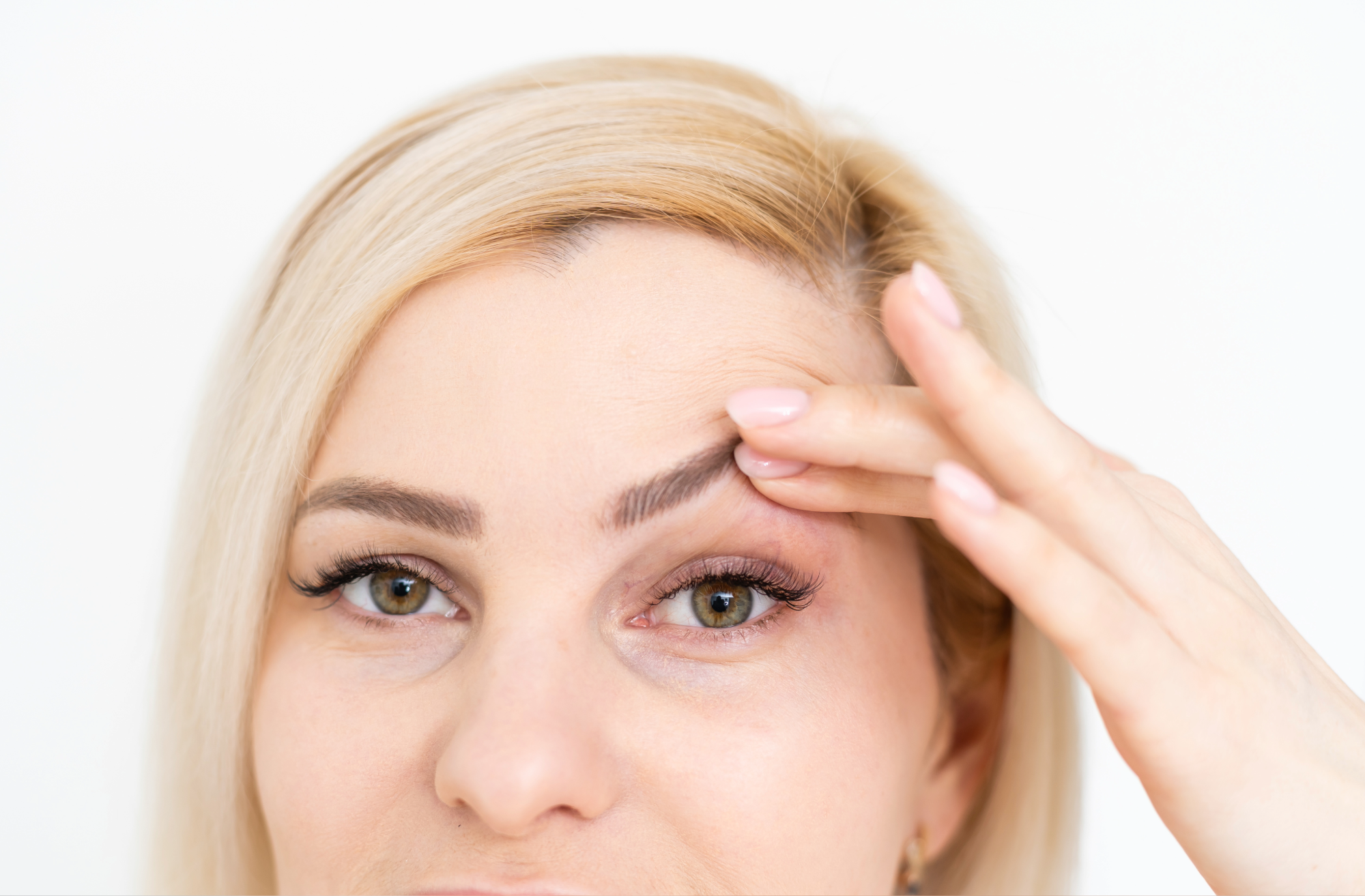 Woman touching eyebrow, demonstrating skincare or beauty routine with focus on eye and hand.