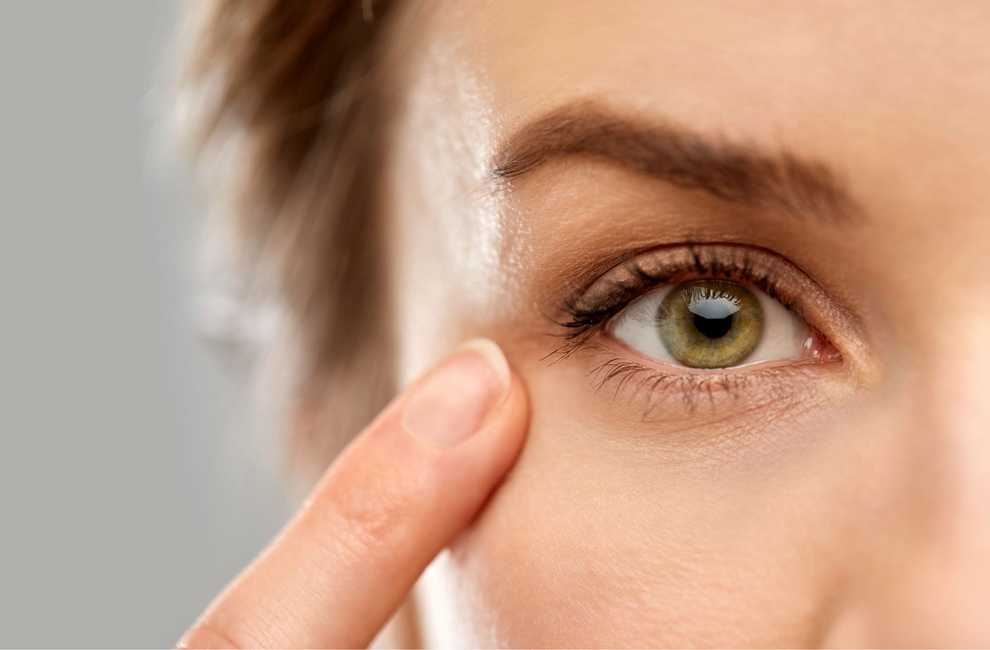 Close-up of a person touching the skin near their eye, highlighting skincare and eye health.