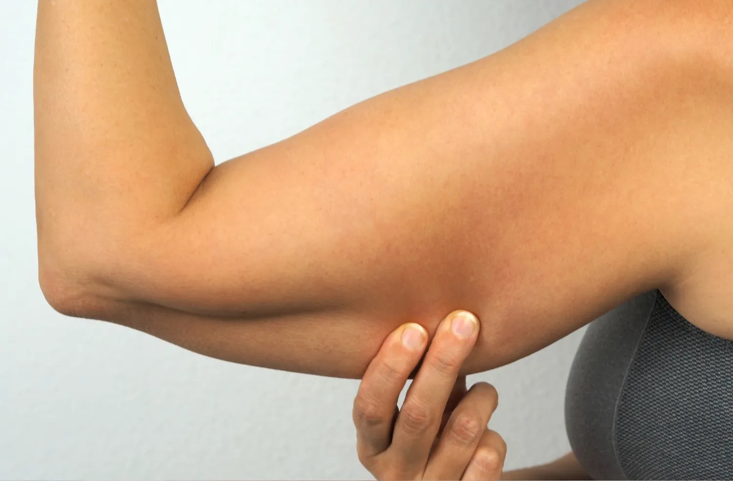 Person pinching loose skin on the underside of their flexed upper arm.