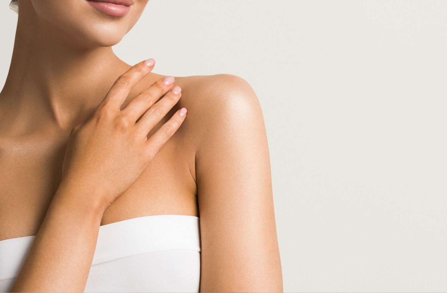 Close-up of a woman’s shoulder and hand with smooth skin, wearing a white strapless top.