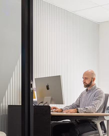Team member seated at a computer in a quiet, naturally lit space, viewed through a partition—emphasizing thoughtful, uninterrupted work time in a modern studio.