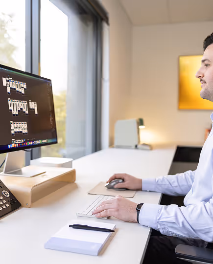 Person seated at a workstation, actively working on a desktop monitor in a softly lit office, showcasing focus and individual creative flow.