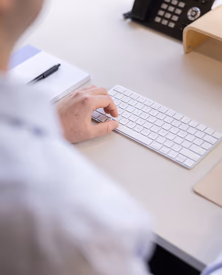 Close-up of a hand using a mouse on a minimalist desk setup with a white keyboard, conveying attention to detail and precision in a digital workspace.