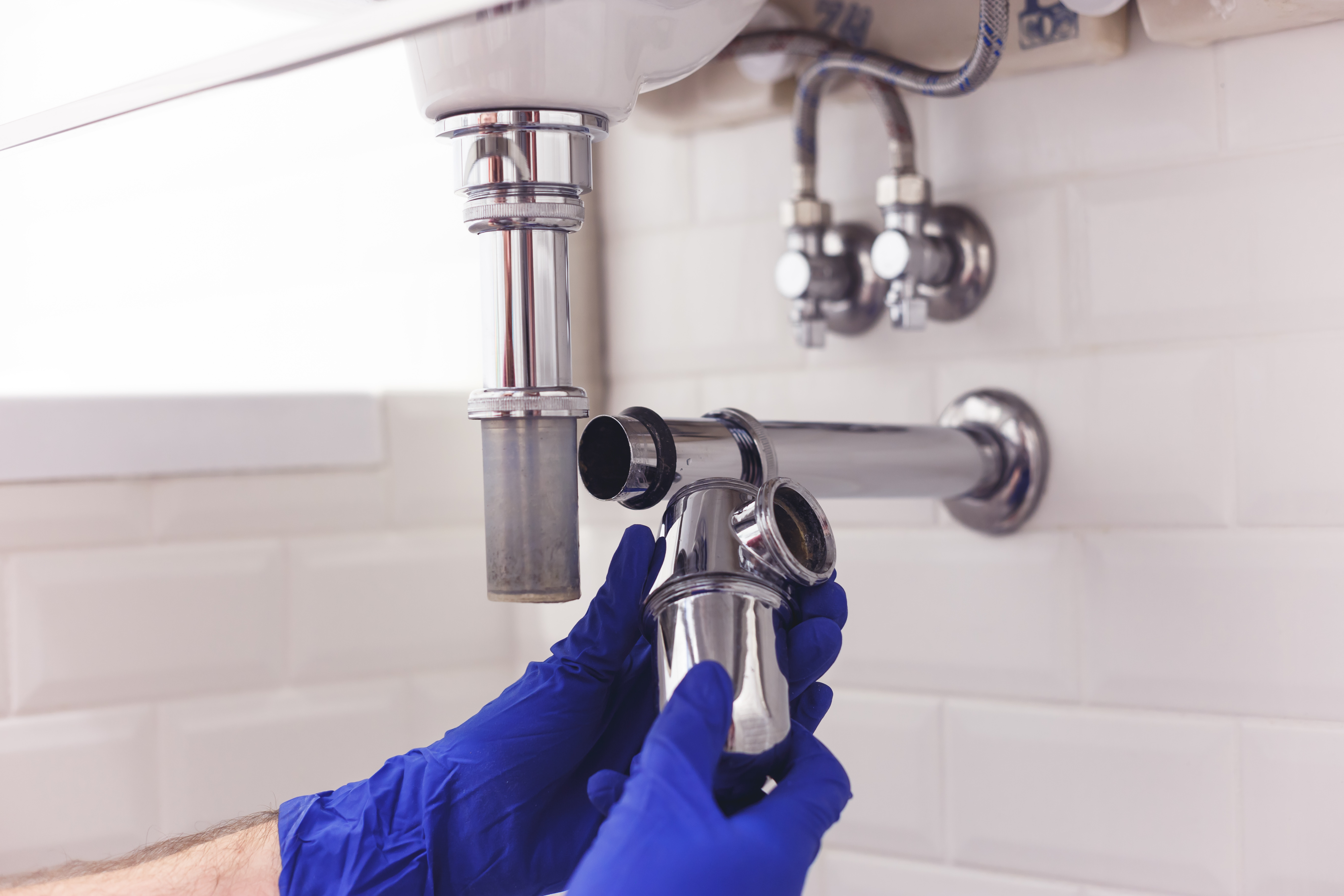 Plumber in blue gloves fixing bathroom sink