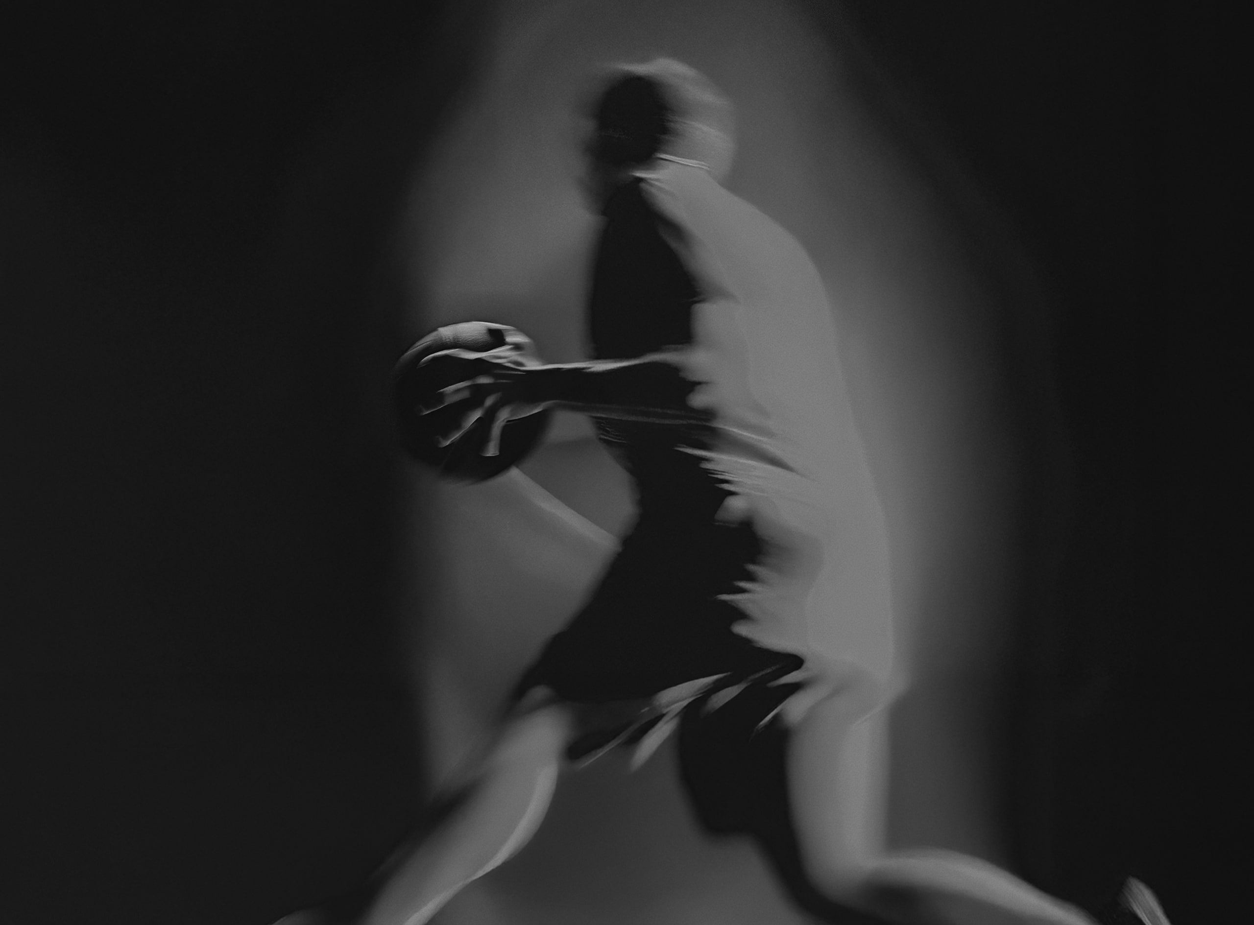 Schwarz-weißes und verschwommenes Bild eines Basketballspielers auf dunklem Hintergrund.
