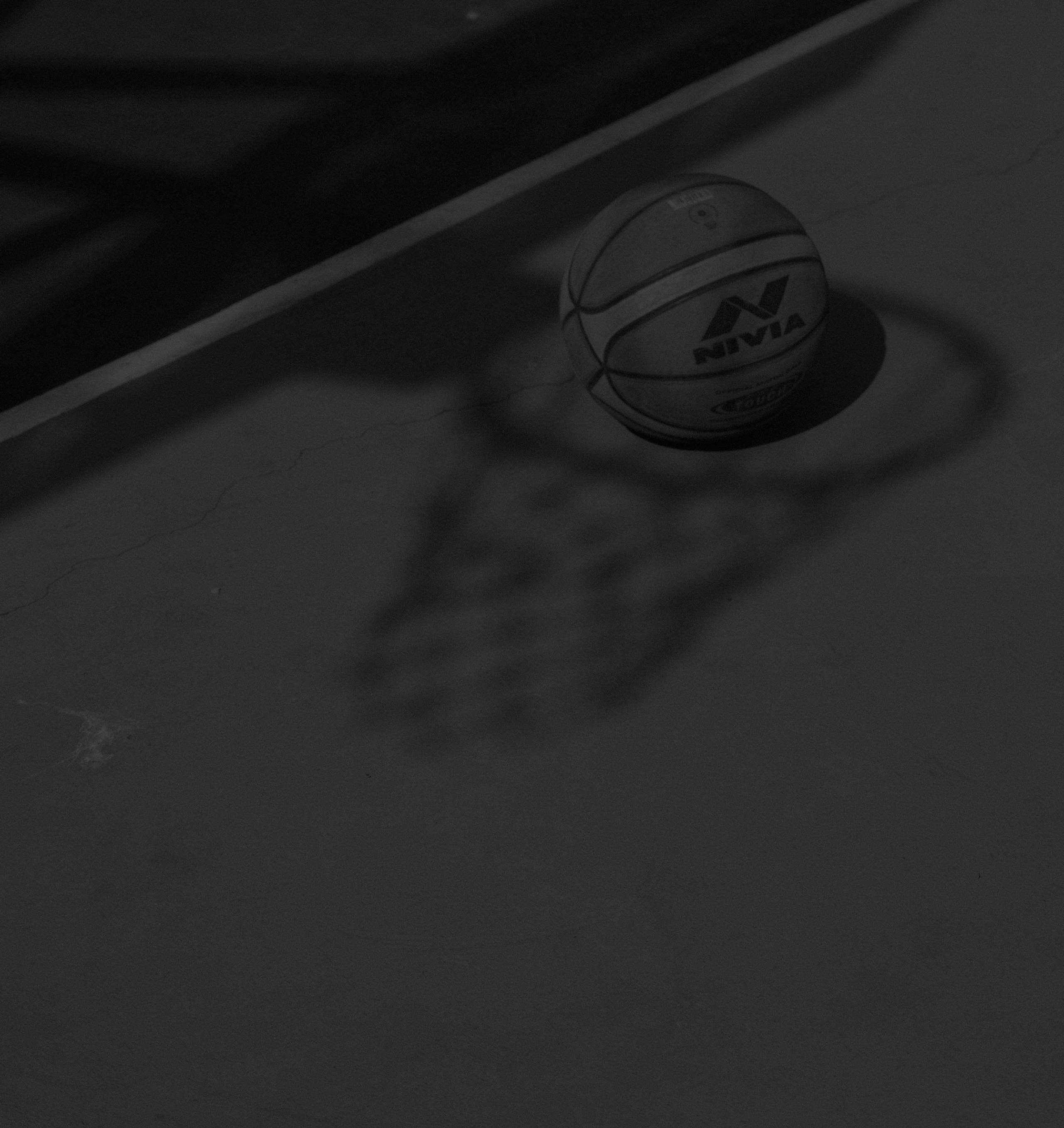Schwarz-weißes Bild von einem Basketball auf einem Outdoor-Court mit Schatten eines Korbs.