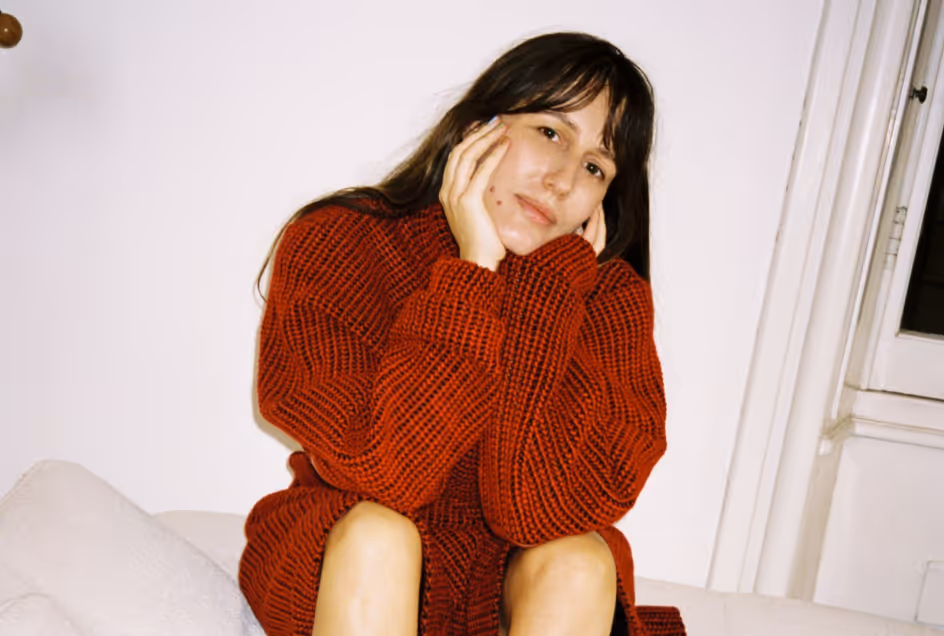 Donna con maglione rosso seduta e sorridente, in un ambiente interno con sfondo neutro.