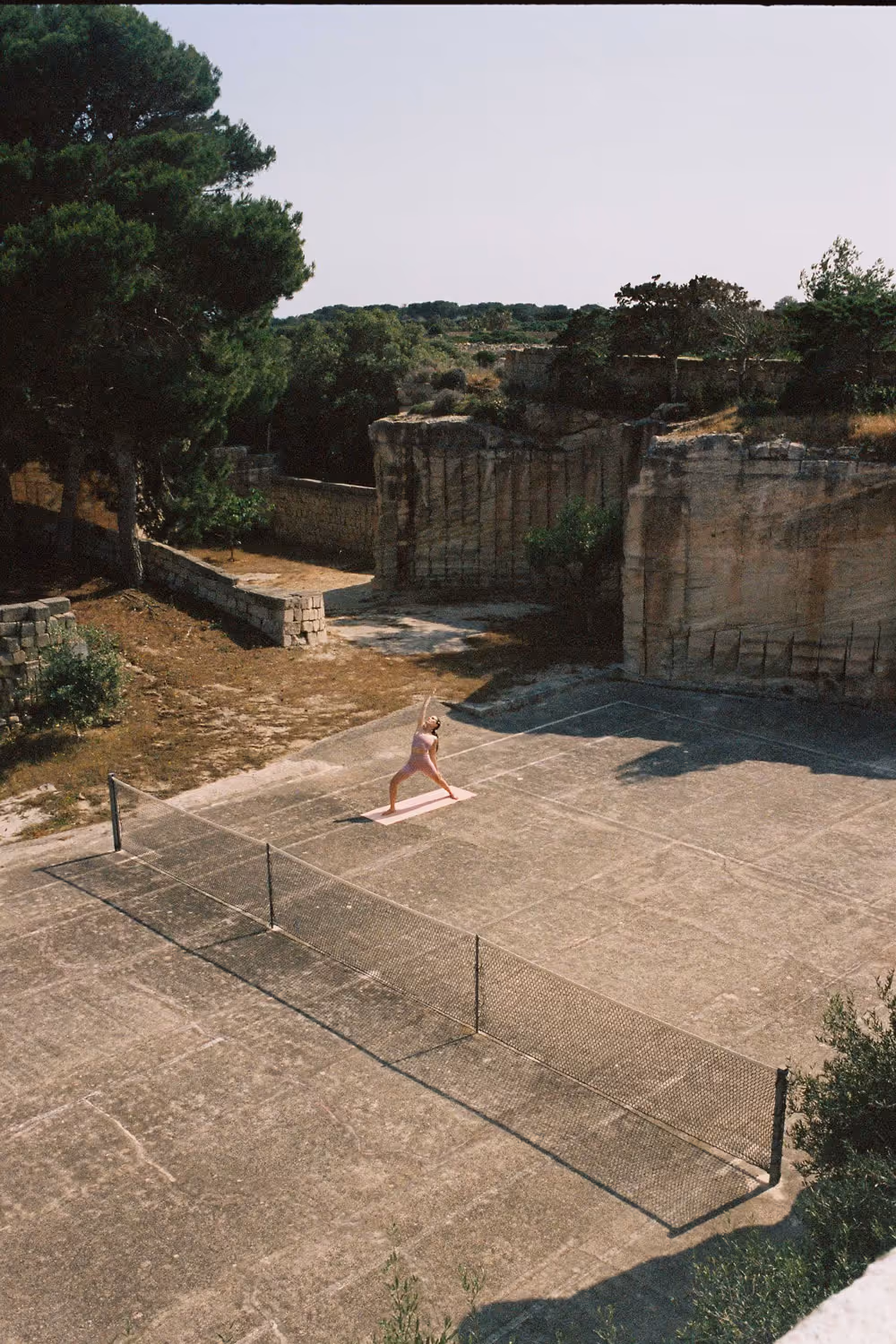 Donna che pratica yoga all'aperto in una posa di allungamento, con sfondo cielo azzurro.