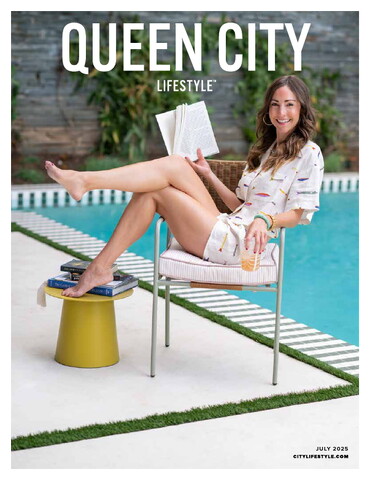 Cover of Queen City Lifestyle, July 2025 issue. A smiling woman lounges poolside in a printed romper, holding a book and a drink. She sits barefoot in a modern chair, with one leg propped on a small yellow side table stacked with books. The relaxed, summery scene evokes leisure and joy.