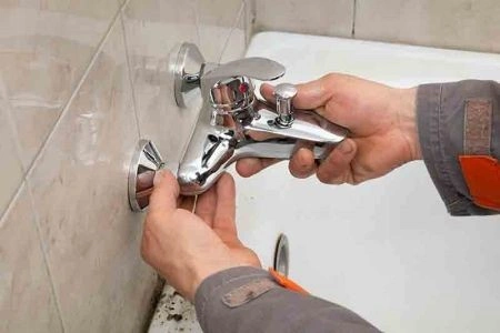 Man fixing a chrome bathroom faucet.