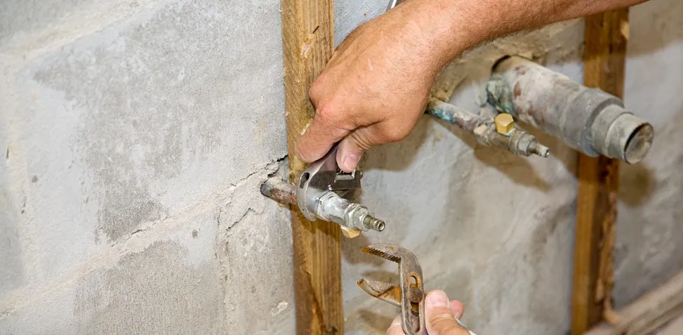 Man fixes old pipes in wall.