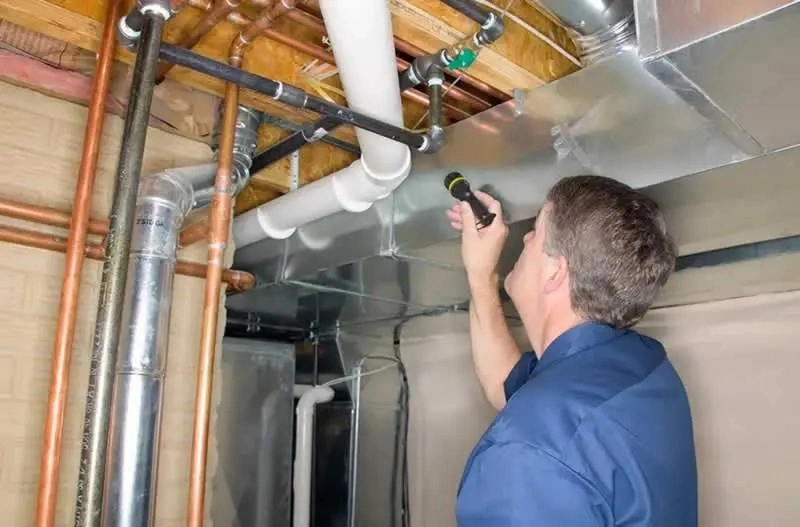 Man inspecting basement plumbing with flashlight.