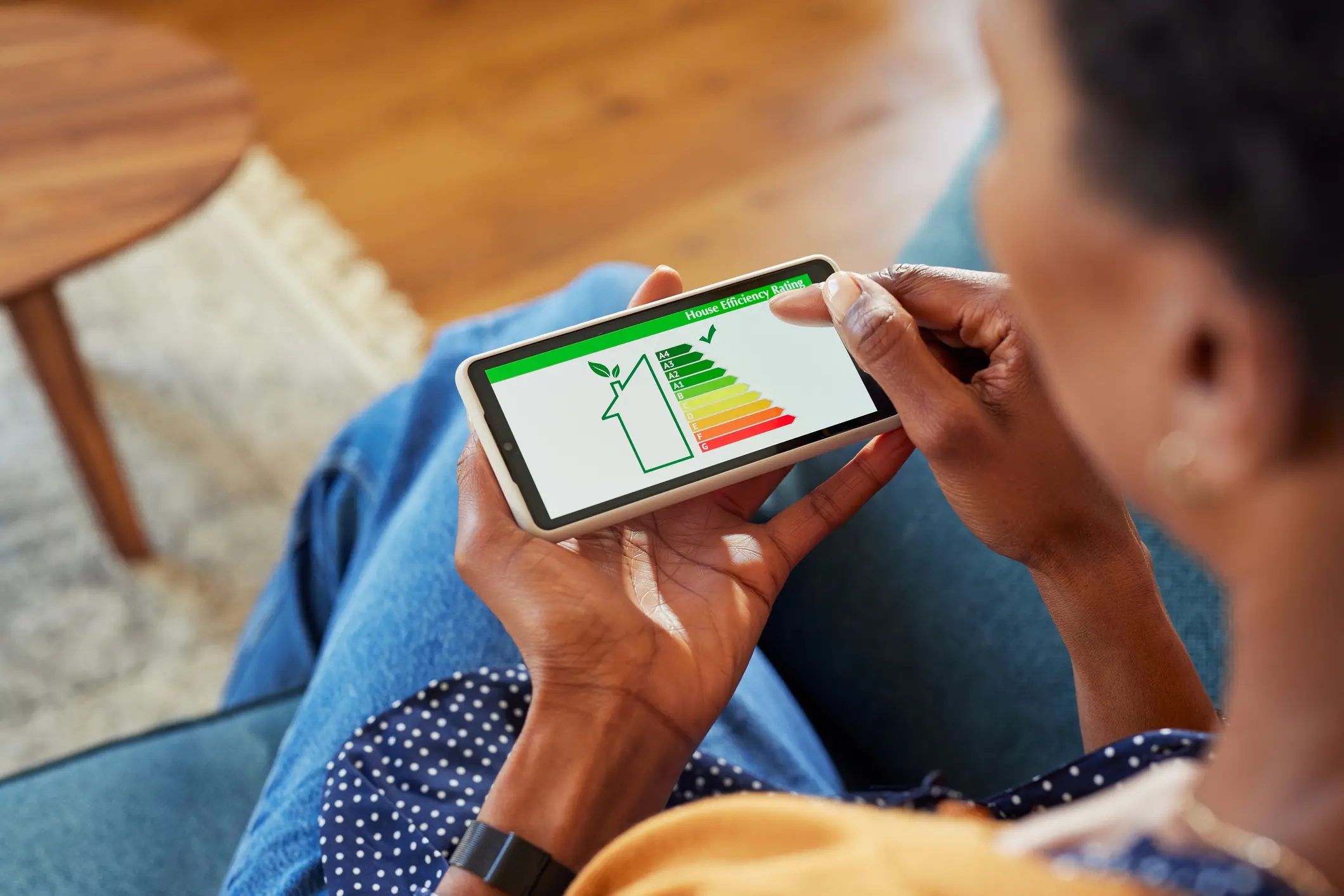 A person holds a smartphone displaying a house efficiency rating with a green-to-red scale, showing an 'A+' rating.