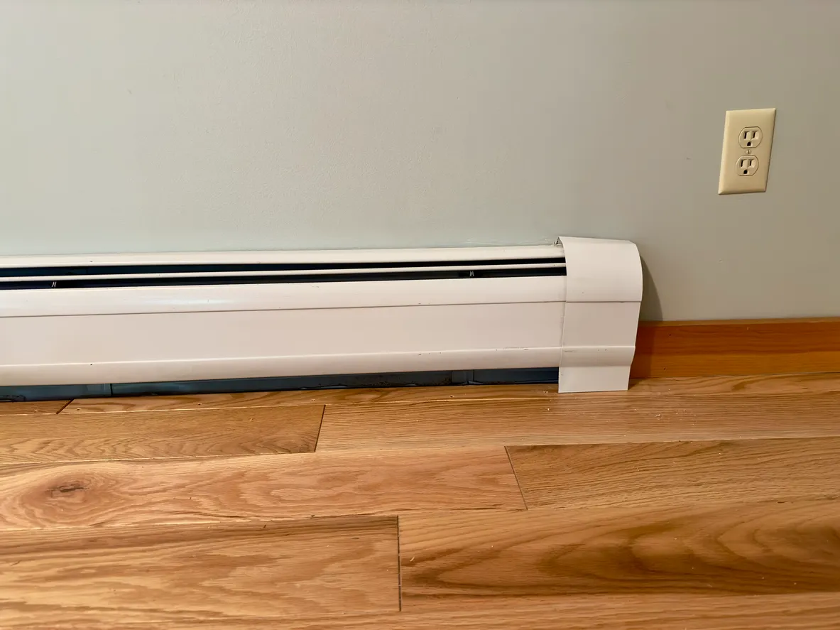 A low-angle view of a white electric baseboard heater along a light blue wall with a wood floor below