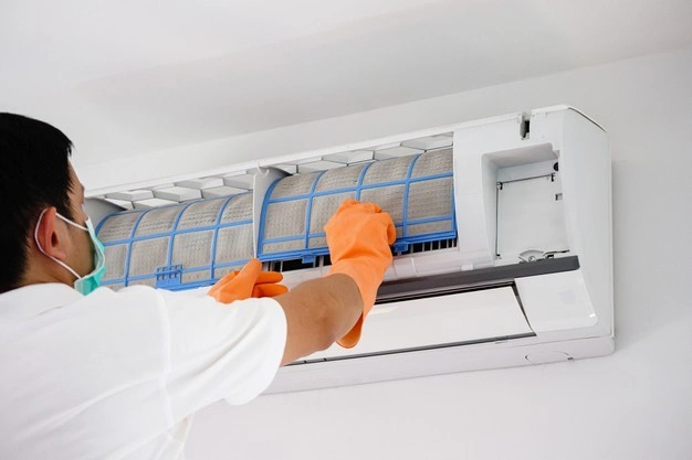 A worker cleaning a dusty AC filter.